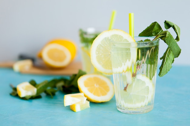 Two glasses with delicious homemade lemonade on gray background sitting on blue desk