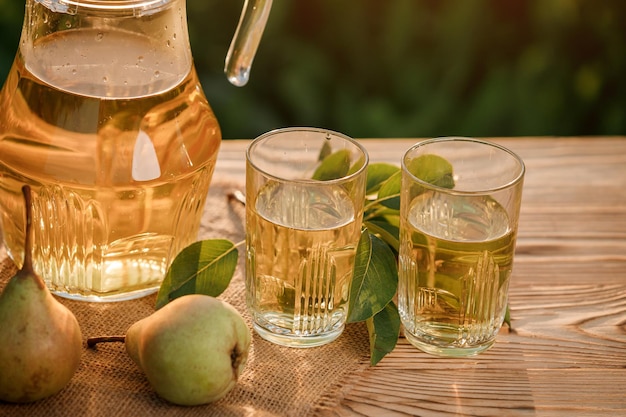 Two glasses with pear juice and basket with pears on wooden
table with natural orchard background on sunset light vegetarian
fruit composition