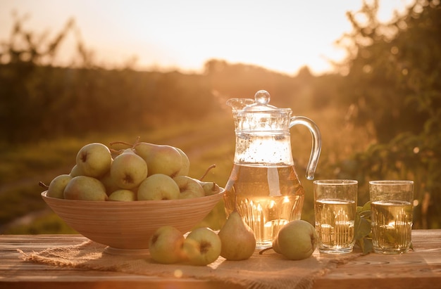 Due bicchieri con succo di pera e cesto con pere su tavola di legno con sfondo naturale del frutteto alla luce del tramonto composizione di frutta vegetariana