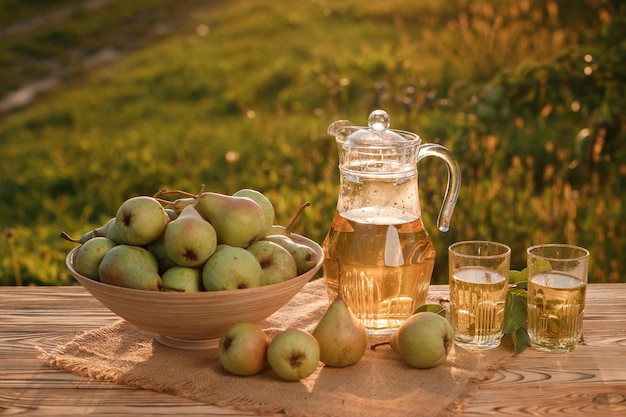 Two glasses with pear juice and basket with pears on wooden table with natural orchard background on sunset light Vegetarian fruit composition