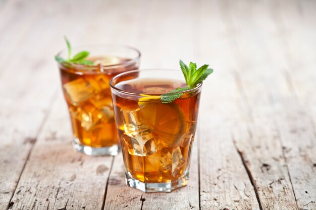 Two glasses with traditional iced tea with lemon, mint leaves and ice cubes in glass