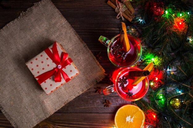 Two glassescup of red hot drinkMulled wine on wooden background with christmas spicesorange sliceclose upChristmas mulled wineBranch of Christmas tree Christmas lights