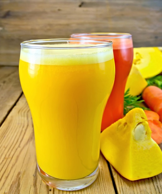 Two glassfuls with pumpkin and carrot juice vegetables on background of wooden boards