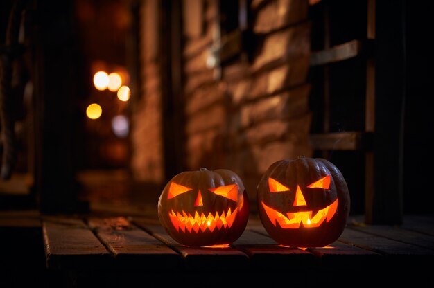 Two glowing Halloween Pumpkins at the entrance to an old wooden house