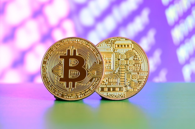 Two gold bitcoins lie on the green surface on the background of the display