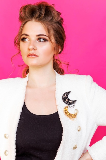 two gold and black moonshaped brooches on the girl's white jacket the girl poses on a bright pink background