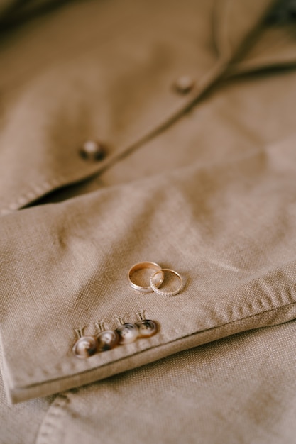 Two gold wedding rings on a beige mens blazer with buttons