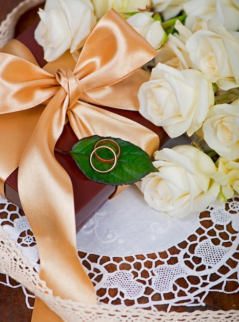 Two gold wedding rings and bouquet of white rose with green leaves on a wooden