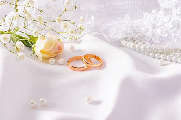  ⁇ 細なベージュ色のサテン背景の上に2つの金色の結婚指輪が横たわっています 婚礼の花束 デザイン モックアップポストカードの招待状 コピースペース