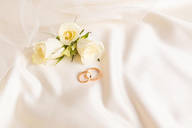 사진 라이브 차 장미와 디자인 웨딩 배경을 위한 신부의 베일 세련된 레이아웃의 일부가 있는 베이지색 새틴 배경에 두 개의 금 결혼 반지