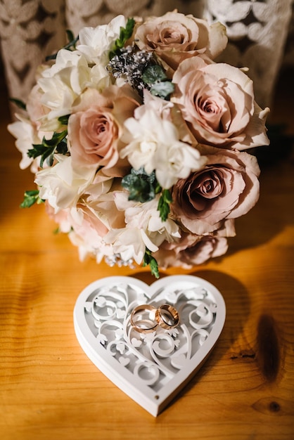 Два золотых обручальных кольца на деревянной шкатулке в форме сердца вид сверху обручальные кольца жениха и невесты помолвка свадебный букет