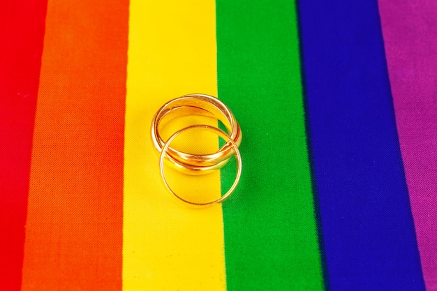 Two gold wedding rings on rainbow lgbt flag.