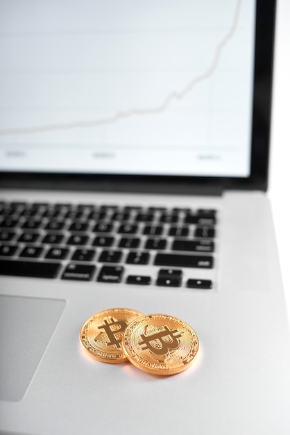 Two golden bitcoins as main cryptocurrencies placed on silver laptop with blurred chart on screen on background.