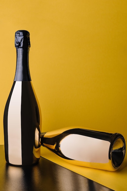 Two golden bottles of champagne on yellow background