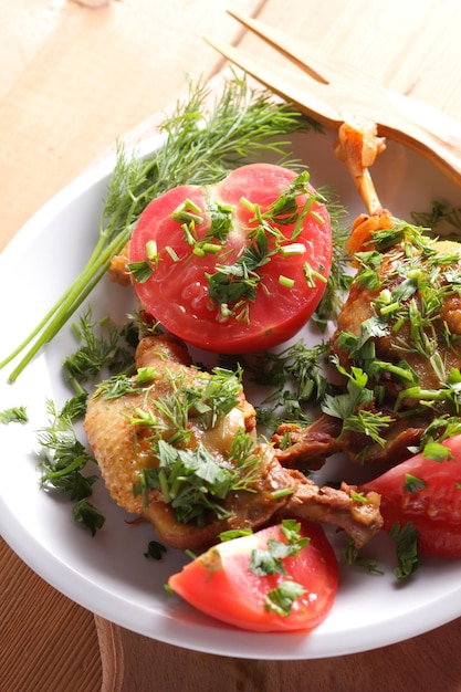 Two golden duck legs with herbs and tomatoes on a white plate on a wooden background Baked duck closeup