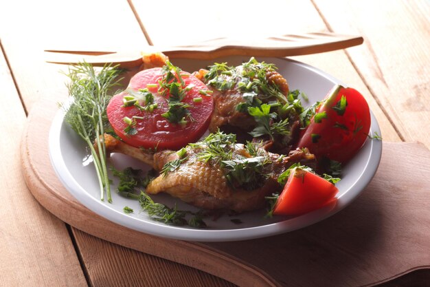 Two golden duck legs with herbs and tomatoes on a white plate on a wooden background Baked duck closeup