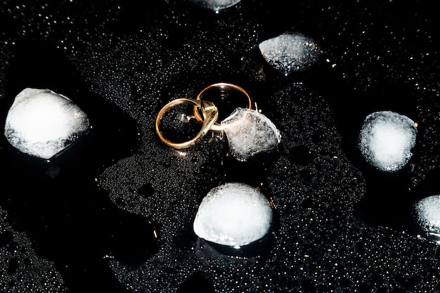 Two golden rings on a black background with drops of water and pieces of ice