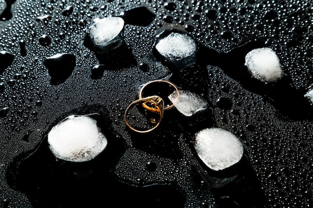 Two golden rings on a black background with drops of water and pieces of ice