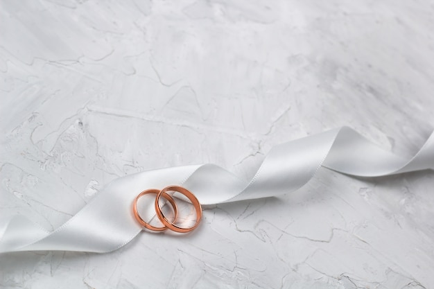 Two golden rings and white satin ribbon wedding decor or wedding invitation background concept