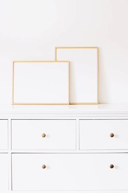 Two golden vertical and horizontal frames on white furniture