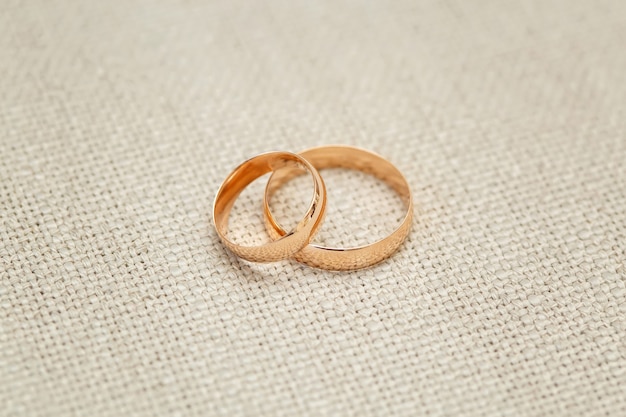 Two golden wedding rings on beige surface, close up