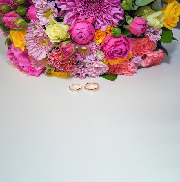 Two golden wedding rings and colorful flowers on white background Wedding background copy space