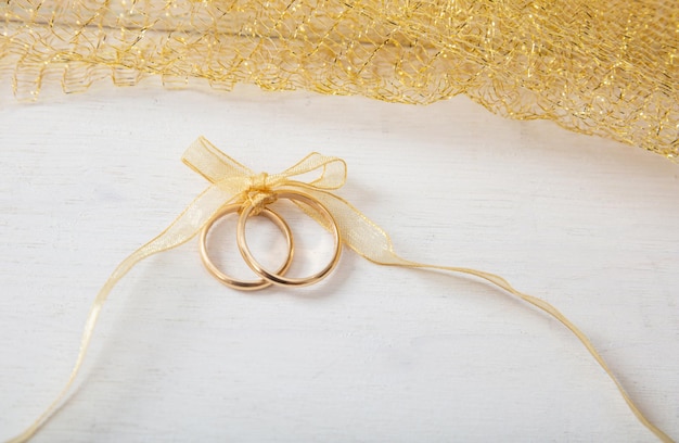 Two golden wedding rings tied with a golden ribbon on white wooden background