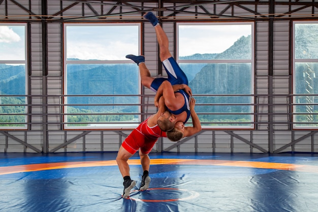 Photo two greco-roman  wrestlers in sportwears makes a throw through the chest  on a wrestling carpet in the gym