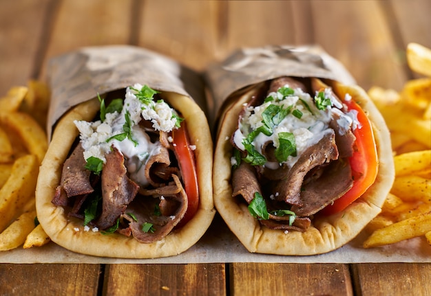 Two greek gyros with seasoned fries on wax paper