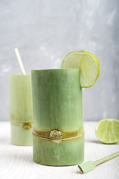 흰색 나무 테이블에 상쾌한 음료와 라임 조각으로 두 개의 녹색 대나무 컵