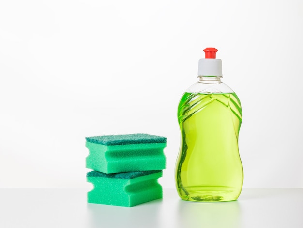 Two green foam sponges and dish washing gel on a white table