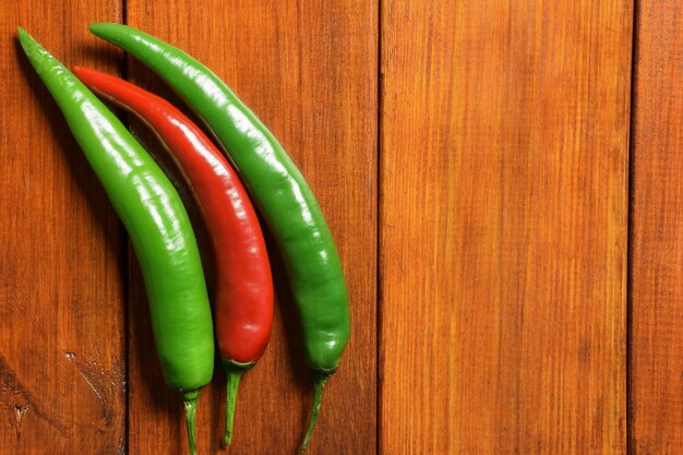 Two green and one red fresh pods of chili peppers lie on the left on a wooden brown table