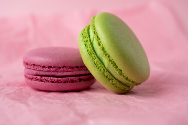 Two green and purple French macaroon cookies lie on a pink paper background. Side view