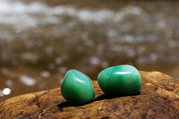 Two green quartz crystals supported on a rocky surface with blurred water in the background