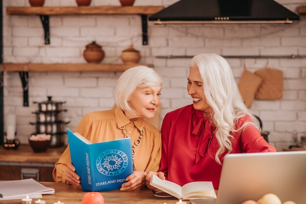 Two grey-haired pleasant cute ladies feeling positive while studying together