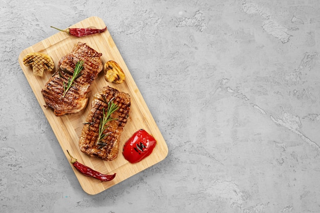 Two grilled beef steaks on wooden board , top view