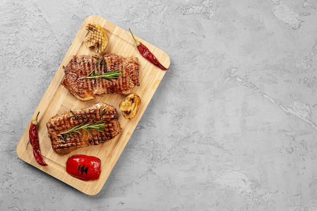 Two grilled beef steaks on wooden board , top view