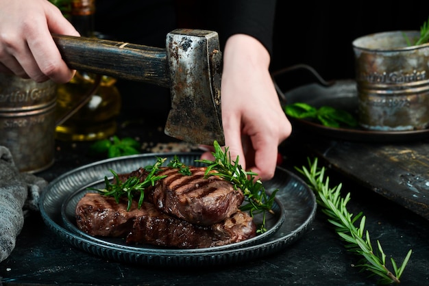 Two grilled ribeye beef steak on a plate in the hands of the chef Food banner On a black background