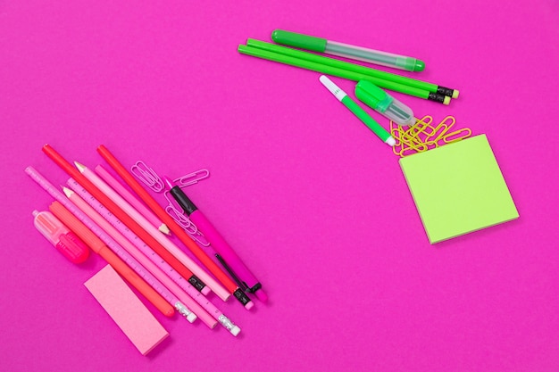 Two groups of pink and bright green office equipment are lying on opposite sides on pink surface isolated