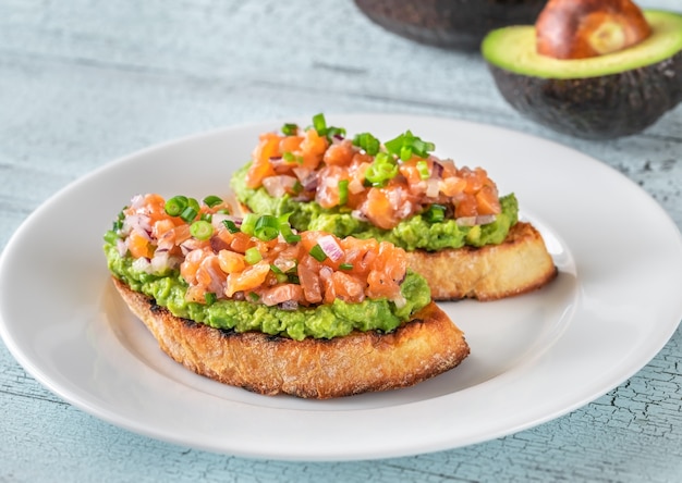 Two guacamole and salmon toasts on white plate