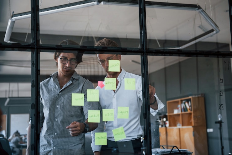Photo two guys in formal clothes stands in the office behind the glass and puts stickers on it.