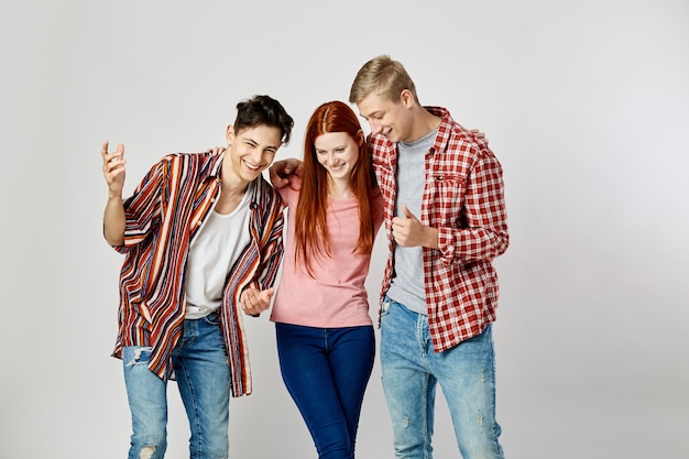 two guys and a girl in stylish bright colorful clothes stand and smile on the white background