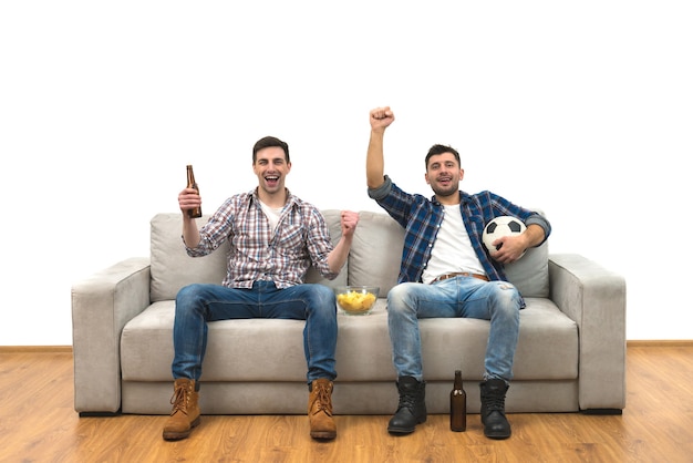 I due ragazzi con una birra guardano una partita di calcio su uno sfondo di muro bianco