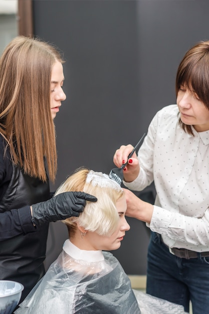 Photo two hairdressers are dyeing hair of woman