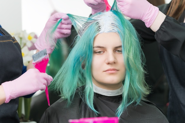 Two hairdressers use pink brush when applying paint to hair during process of bleaching hair roots