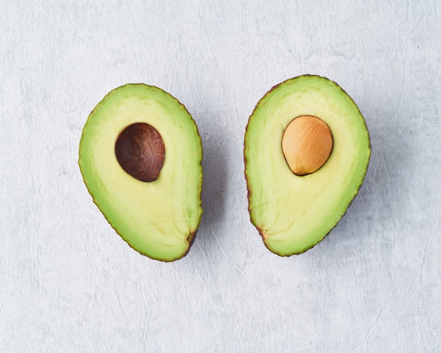 Two half avocado with seed on gray concrete table background.