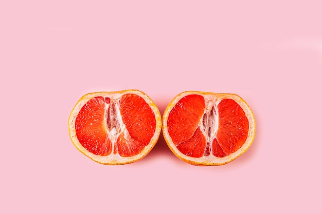 Two half of fresh red cut grapefruit on pink surface. Female health concept. Fruit as symbol of vagina. Close up.