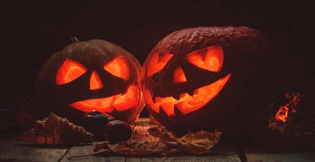 Two Halloween pumpkin JackoLantern on dark wooden background with fallen leaves and flames selective focus and toned image