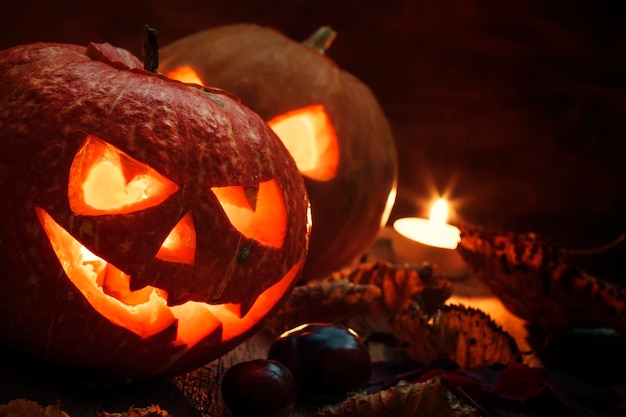 Two Halloween pumpkin JackoLantern on dark wooden background with fallen leaves and flames selective focus