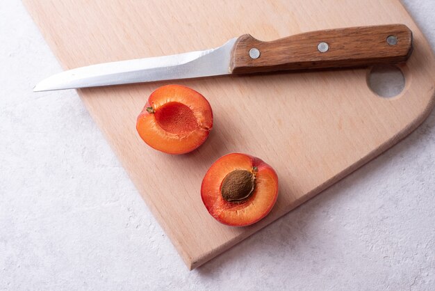 Two halves of apricot on a cutting board with a knife on a white background, healthy food concept, close up.